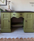 Green painted desk makeover with a black top and bronze pulls. Staged with a stack of books and a vase with flowers on top.