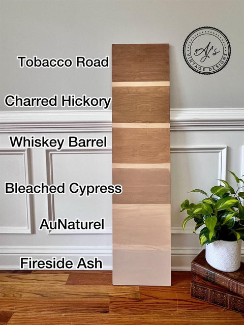 Wooden plank samples in six different shades are displayed vertically. Starting from the top: Tobacco Road, Charred Hickory, Whiskey Barrel, Bleached Cypress, AuNaturel, and Fireside Ash. A potted plant and basket are nearby.