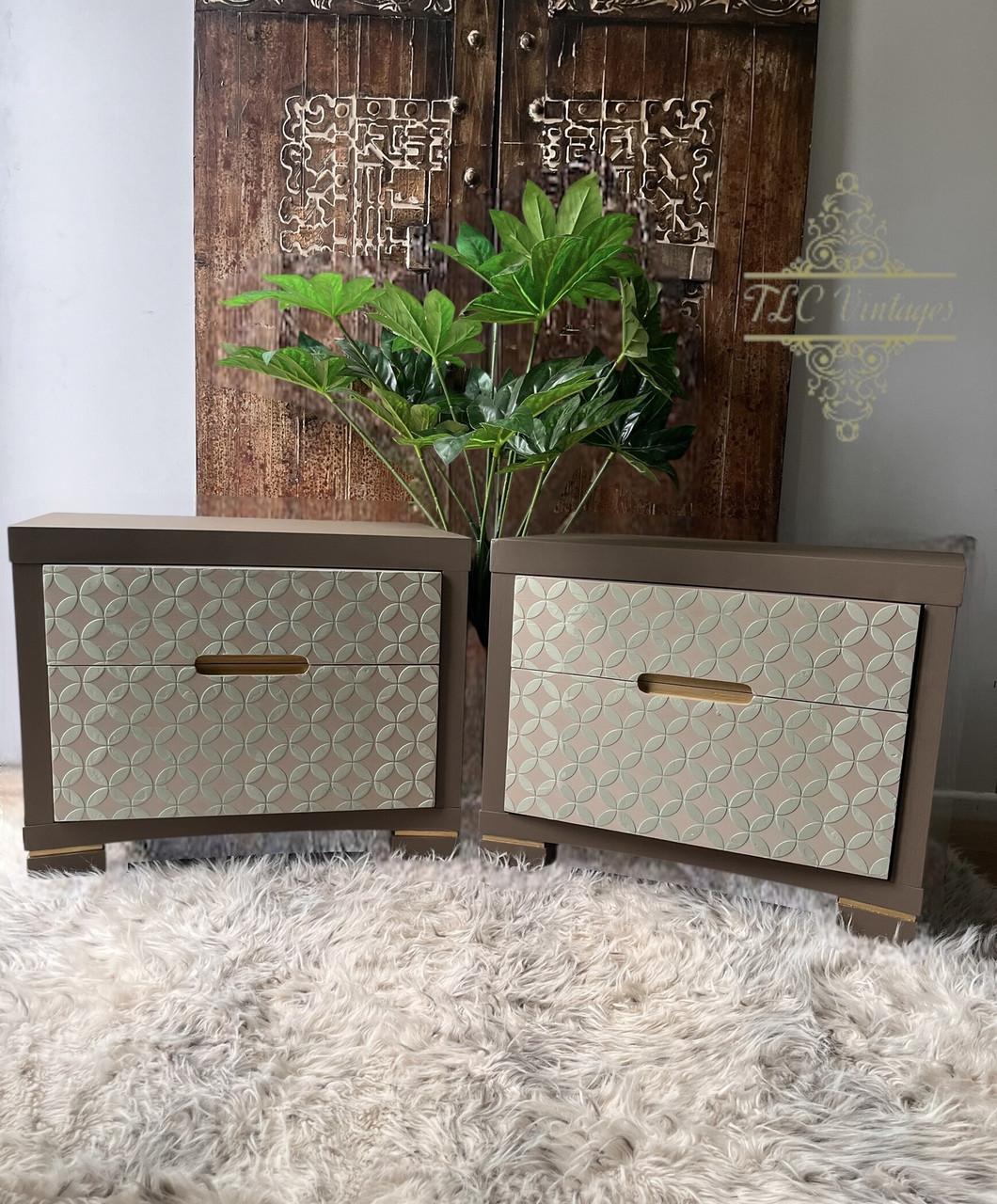 Two modern nightstands with geometric, textured fronts and inset handles sit side by side on a fluffy beige rug. Green plants and a carved wooden door serve as the background decor.