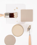 A flat lay of neutral-colored paint samples, a round paint can, a paintbrush, a palette knife, and paint swatches arranged neatly on a white background.