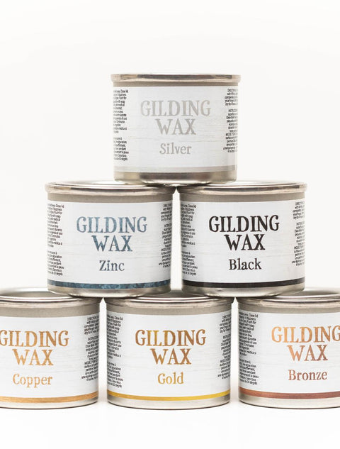 Six cans of gilding wax are stacked in a pyramid. Top row: Silver. Middle row: Zinc, Black. Bottom row: Copper, Gold, Bronze. Each can has a white label with detailed text around the name.