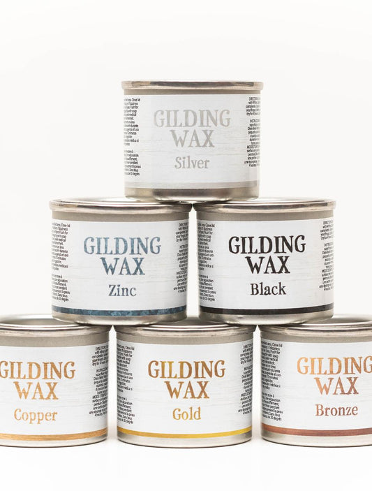 Six cans of gilding wax are stacked in a pyramid. Top row: Silver. Middle row: Zinc, Black. Bottom row: Copper, Gold, Bronze. Each can has a white label with detailed text around the name.
