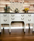 Grayish white painted dresser makeover with dark brown feet and top and bronze pulls. Staged with candlesticks, a picture frame and sunflowers on top.
