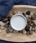 Overhead shot of an open jar of Glacier. Staged in a wooden bowl with rocks on a navy blue sheet.