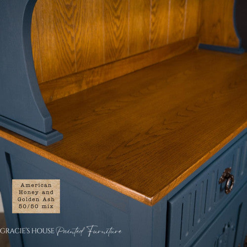 A close-up of a wooden cabinet with a blue painted body and a warm golden-brown wood top. A label reads “American Honey and Golden Ash 50/50 mix.” Gracie's House Painted Furniture watermark is at the bottom.
