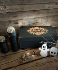 Black painted box with the spiderweb Happy Halloween Stencil design applied in goldish orange. Small white ghost figurine, small white skull figurine, two small black candle holders with orbs inside.