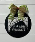 Black painted circular sign with the spiderweb and spider Happy Halloween Stencil design applied in white. Green and white striped bow on the top of the sign.