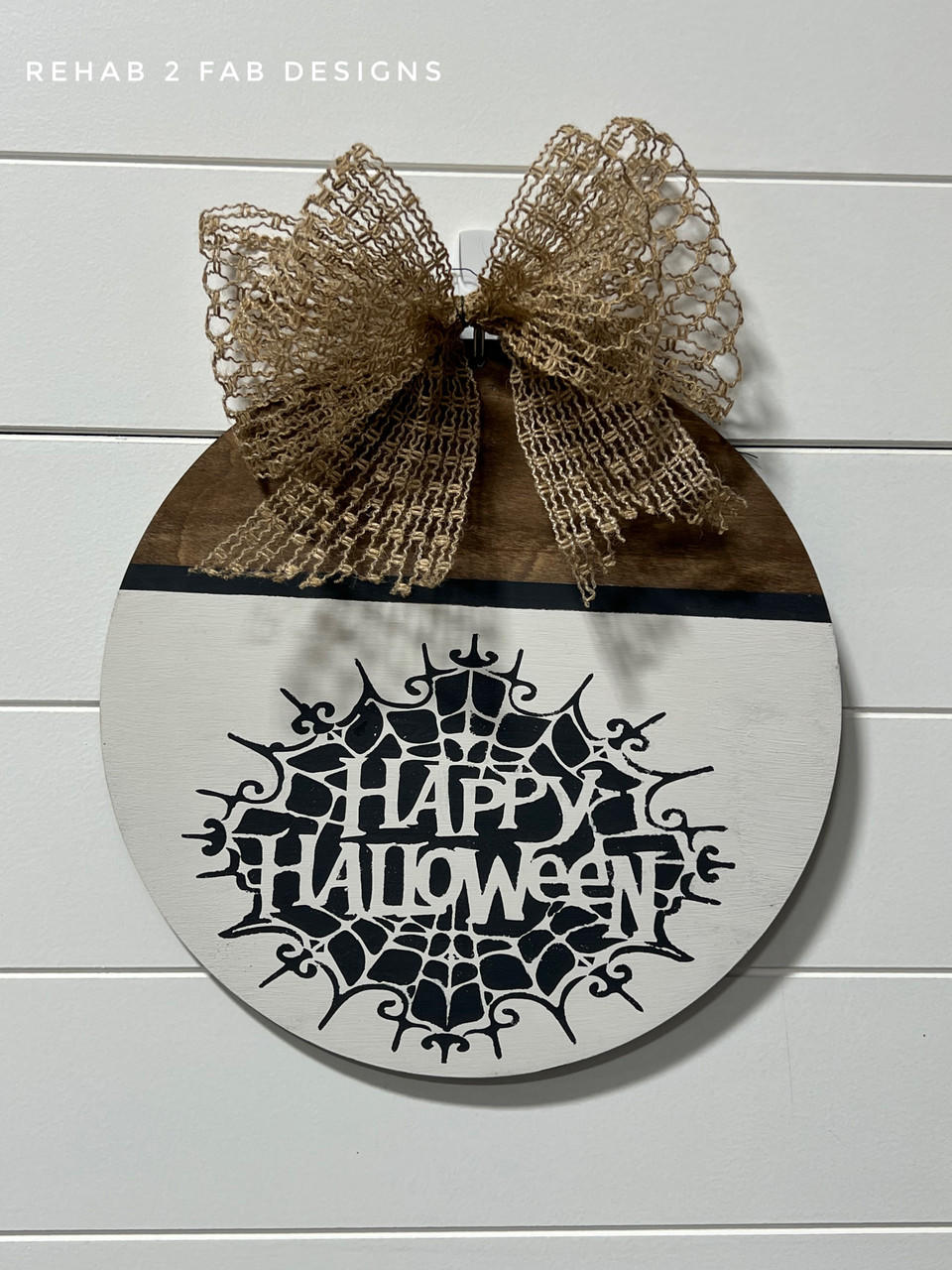 Half natural wood, half white painted circular sign with the spiderweb Happy Halloween Stencil design applied in black. Burlap bow on the top of the sign.