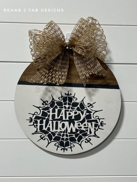 Half natural wood, half white painted circular sign with the spiderweb Happy Halloween Stencil design applied in black. Burlap bow on the top of the sign.