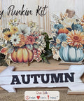 Two autumn-themed pumpkin floral arrangements and a white wooden arrow sign labeled "AUTUMN" are displayed on a wooden surface. Text at the top reads "Hey Punkin Kit." The background has a rustic, light wood texture.