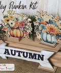 Two autumn-themed floral pumpkin decorations sit on a wooden box with foliage, next to a white wooden arrow sign reading "AUTUMN." Text above reads "Hey Punkin Kit."