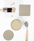 Flat lay of a paintbrush with green paint, a glass sheet with green paint drops, an open can of green paint, two green color samples, and a palette knife with green paint on a white background.