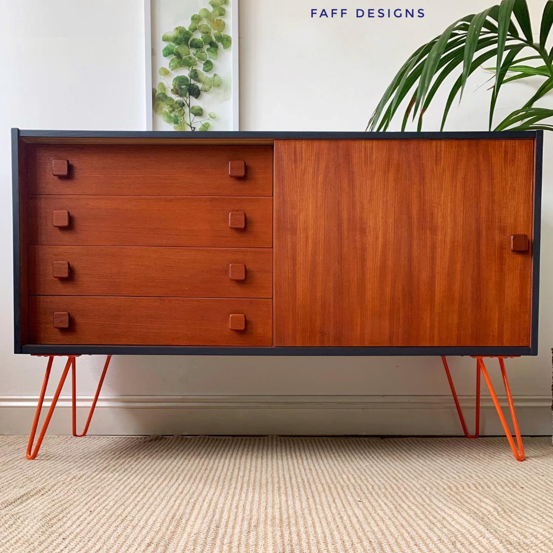 A wooden sideboard with four drawers and a cabinet door, featuring square handles. It stands on orange metal hairpin legs. A green leafy plant and framed leaf art are in the background. The words "FAFF DESIGNS" are at the top right.