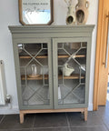 A curio cabinet that has been painted with chalk paint, staged with clay pottery and a glass front.