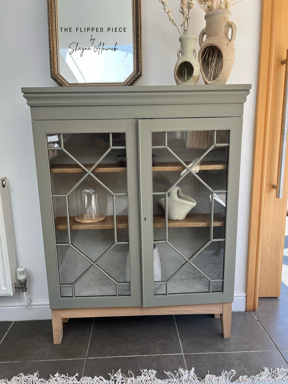 A curio cabinet that has been painted with chalk paint, staged with clay pottery and a glass front.