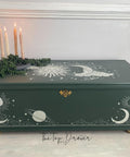 Dark green painted chest with a gold hinge and gold feet. The Lani's Celestial Dream Transfer has been applied on the top and the front of the piece. Staged with a dark green platter with faux string of pearls strown across the top and 4 lit candlesticks.