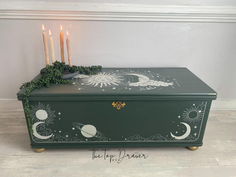 Dark green painted chest with a gold hinge and gold feet. The Lani's Celestial Dream Transfer has been applied on the top and the front of the piece. Staged with a dark green platter with faux string of pearls strown across the top and 4 lit candlesticks.