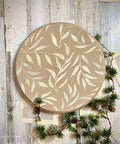 Tan painted lazy susan with the Leaf Me Alone stencil applied in white. Staged with book pages and a garland with small pinecones.
