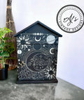 Black chalk painted birdhouse with the Lunar Solstice Transfer applied to the front and the door. With a gold pull. Staged next to a pothos plant.