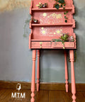 Pink painted tall shelf with the Lunar Solstice Transfer applied on the middle back of the piece and outlined in gold. Staged with faux succulents in one of the drawers and small pots with plants hanging over the edge on the shelves.