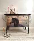 Black and gray painted dresser with the Majestic Horse decoupage paper applied on the front. Staged with 2 lit candlesticks on the dresser and 1 on the floor with book pages strewn on the floor.
