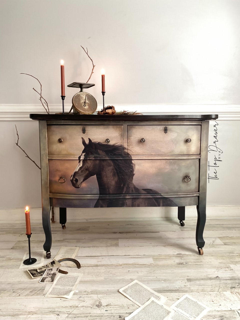 Black and gray painted dresser with the Majestic Horse decoupage paper applied on the front. Staged with 2 lit candlesticks on the dresser and 1 on the floor with book pages strewn on the floor.