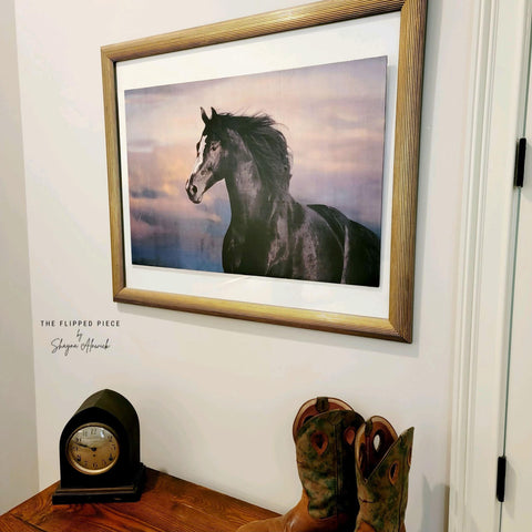 Majestic Horse decoupage paper in a gold frame, hung on the wall. Staged with cowboy boots and an old clock on the table below it.