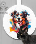 A colorful painted image of a happy dog is displayed on a circular white background mounted on a wall. A black cat sits in the foreground, looking upwards. The text "Low Flying Angels" is visible on the left side of the image, alongside a logo of flying cows.