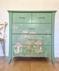Green chalk painted dresser. 9 mushrooms with greenery, and a moon and stars on the top two drawers, applied with the Moonlit Mushrooms Stencil. The mushrooms are variations of purple, pink, green, and white.