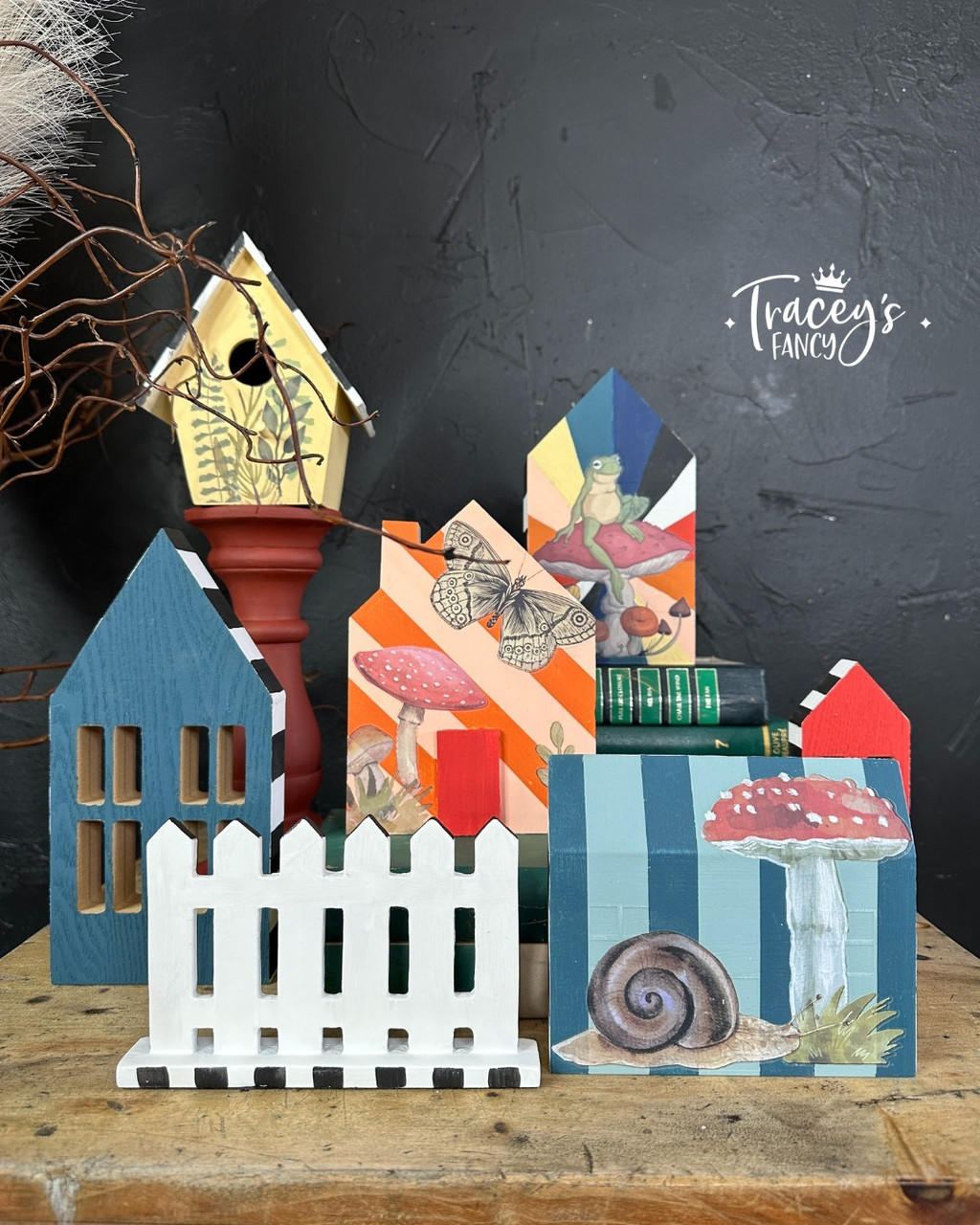 Five little painted house cutouts and a yellow birdhouse along with a white picket fence cutout. Mr. Toad's Transfer has been applied to the front of the house and birdhouse.