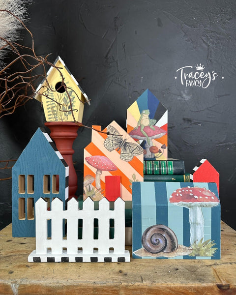 Five little painted house cutouts and a yellow birdhouse along with a white picket fence cutout. Mr. Toad's Transfer has been applied to the front of the house and birdhouse.