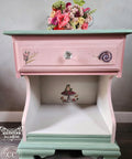 Pink, white, and green painted nightstand. Mr. Toad's transfer has been applied inside of the nightstand and on the drawer. Staged with a flower bouquet on top.