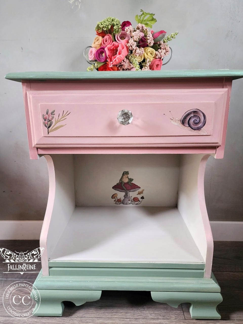 Pink, white, and green painted nightstand. Mr. Toad's transfer has been applied inside of the nightstand and on the drawer. Staged with a flower bouquet on top.