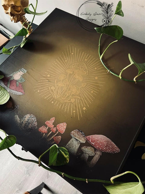 Brownish black painted furniture blended with some tan in the middle. The Cottagecore Mushrooms Silkscreen Stencil has been applied to the center. Mr. Toad's Happy Place Transfer has also been applied to the top of this piece. Vines of a pothos plant spread out on top of the piece.