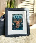 A framed artwork featuring National Parks A3 Rice Decoupage Paper with a stylized stag and the words "National Park, Wild Zone, Estd. 1987, Camping" is displayed against a cozy background with a navy blue and white patterned textile and a fluffy white surface, suggesting a homey, rustic decor vibe.