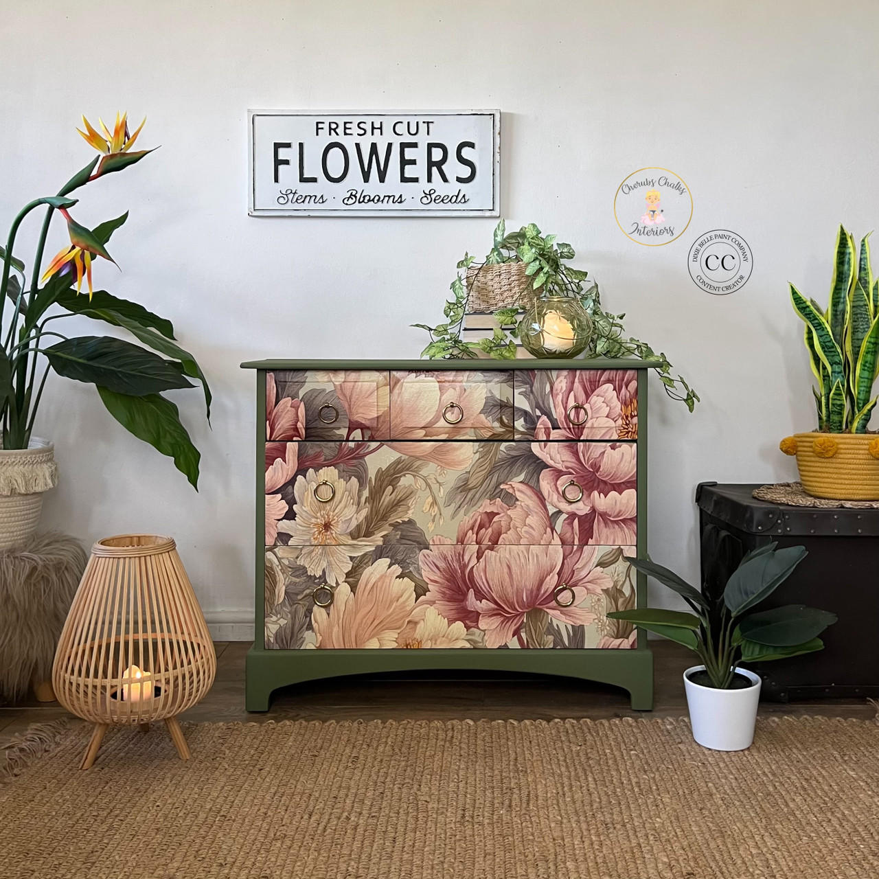 A cozy room corner featuring a green painted dresser with the Peaceful Peonies Decoupage Paper applied on the front. A sign reading "fresh cut flowers, stems - blooms - seeds," a small round table with plants, a lit lamp, and a potted plant on a mat.