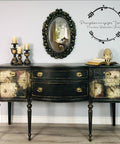 Vintage-style sideboard with floral patterns and ornate drawer handles, below an oval mirror. Candles and a decorative pineapple sit atop. A watermark in cursive script decorates the wall.