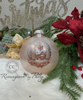 A Christmas ornament with a snowy village scene is displayed among pine branches, red poinsettias, and a golden "Christmas" sign in the background. The ornament features a church and trees dusted with snow.