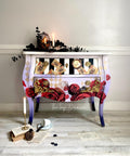 White, black, and purple chalk painted nightstand. The top drawer has been painted with white and black stripes. The Roses are Red Transfer has been applied to the front of the nightstand and on the two drawers. The Harlequin Stencil has been applied in gold.