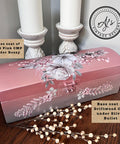 A pink and silver decorative box with white and pink flowers sits on a table. Two white candles in ornate holders are behind it. Text notes the box’s base coats: “Soft Pink CMP under Rozay” and “Driftwood CMP under Silver Bullet.”.