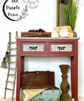 Red painted entryway table makeover with white stenciled drawer fronts and a white stenciled top. Staged with a stack of books on top and a small wooden ladder next to the piece.