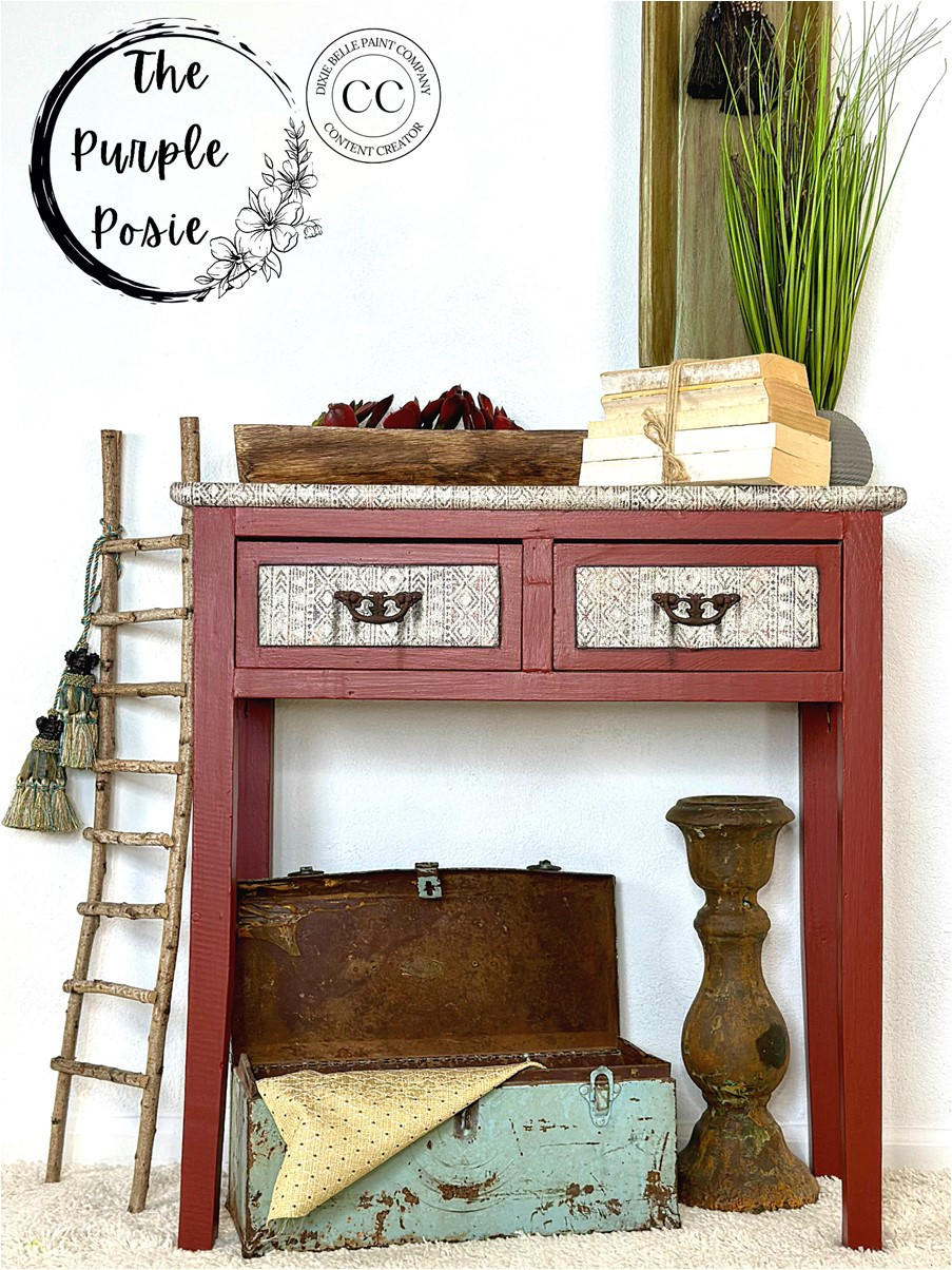 Red painted entryway table makeover with white stenciled drawer fronts and a white stenciled top. Staged with a stack of books on top and a small wooden ladder next to the piece.