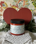 Red painted wooden heart with a jar of Sequoia in front of it. Staged on crocheted lace with faux greenery.