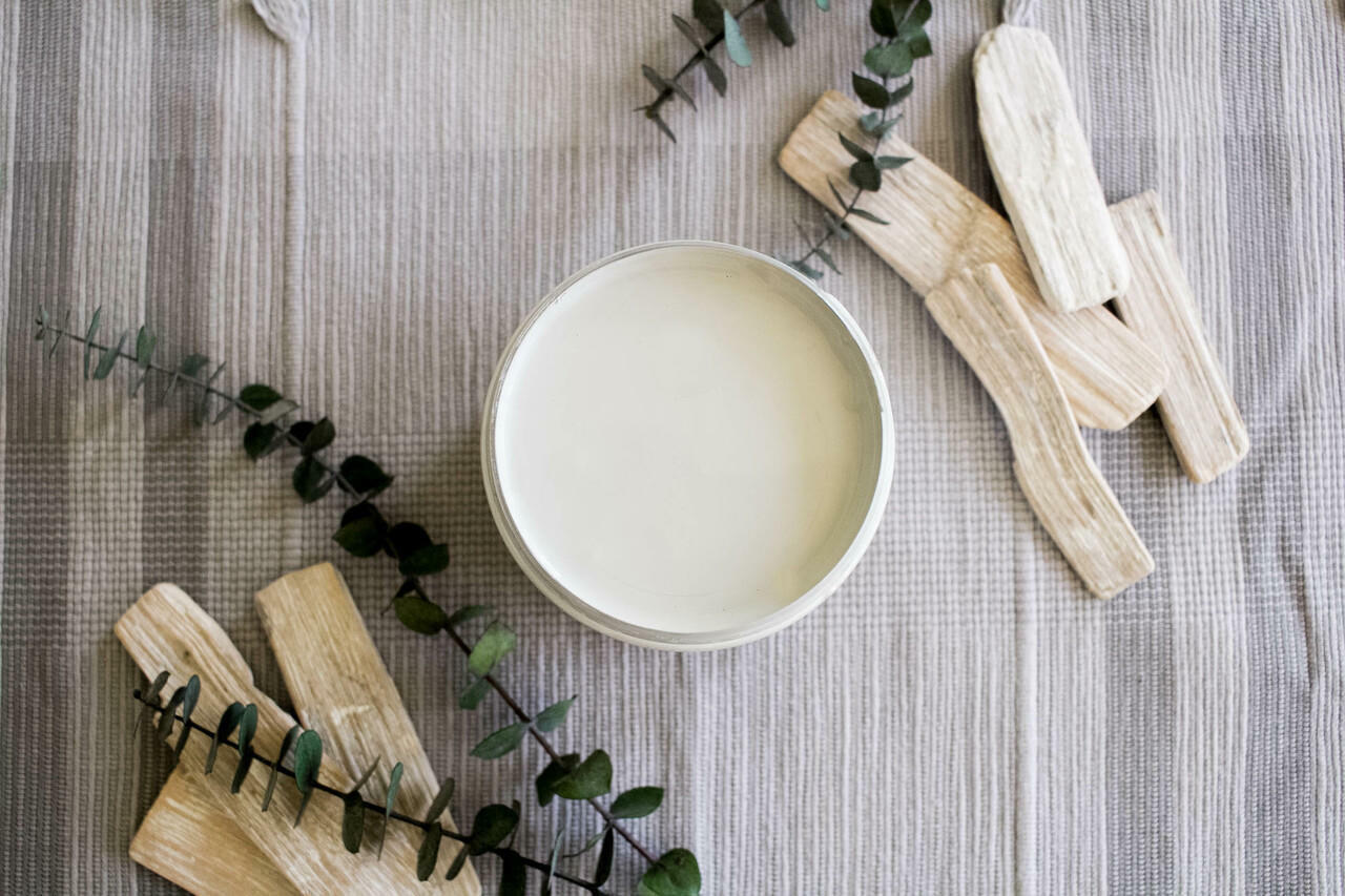 Baja Gray Silk All-In-One Mineral Paint is perfect for painting kitchen cabinets, bathroom cabinets and painting furniture. Image shows a top view of an opened container of  Baja Gray Silk All-In-One Mineral Paint staged on a plaid tablecloth with sticks of palo santo and green branches.