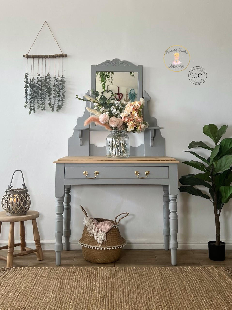 Baja Gray Silk All-In-One paint is perfect for painting kitchen cabinets, bathroom cabinets and painting furniture. This image shows Baja Gray Silk All-In-One Mineral Paint on a one drawer vanity with gold hardware and a natural wood top. There is a small stool next to the vanity along with a plant and a container holding a blanket. A flower arrangement sits atop the vanity to complete the piece.