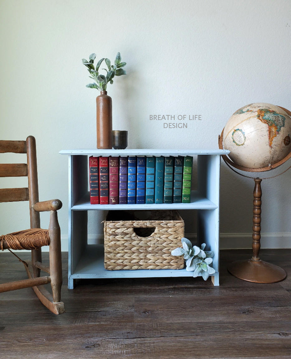 Bay Breeze Silk All-In-One paint is perfect for painting kitchen cabinets, bathroom cabinets and painting furniture.
Beautiful end table painted in Bay Breeze Silk Paint staged with red,blue and green books on the top shelf and a woven box with greenery on the bottom shelf. On a wooden floor with a tall bronze globe on one side and brown wooden chair on the other side.