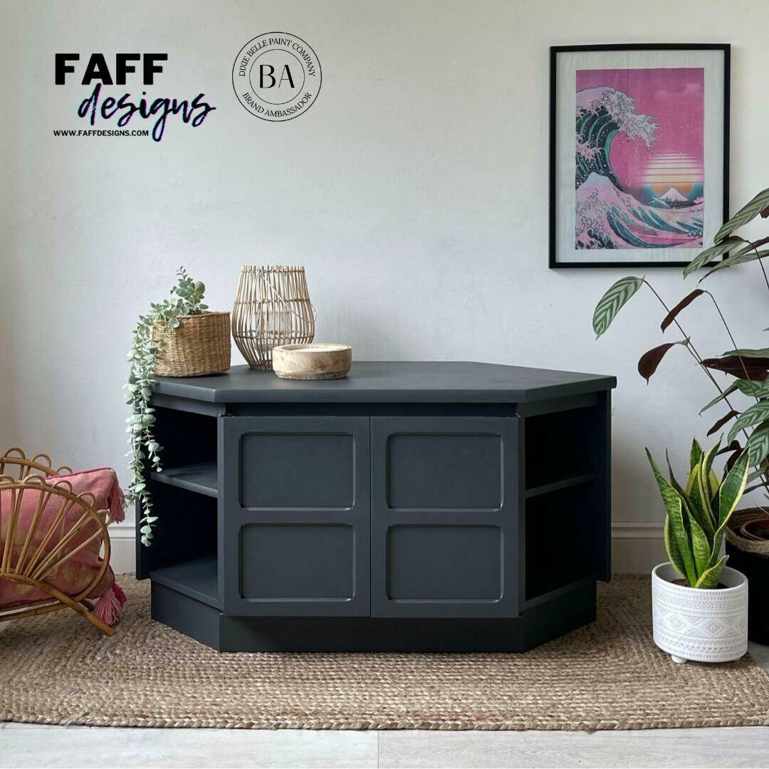 Black Sands Silk All-In-One paint is perfect for painting kitchen cabinets, bathroom cabinets and painting furniture. Entertainment center painted with Black Sand Silk all in one mineral paint. Staged on top of a brown rug, In front of white wall with a wave and sunset picture hanging in a frame. Woven basket with faux succulent plant in it hanging out and over furniture.  White planter with snake plant next to piece.