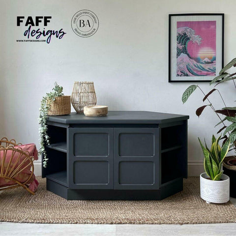 Black Sands Silk All-In-One paint is perfect for painting kitchen cabinets, bathroom cabinets and painting furniture. Entertainment center painted with Black Sand Silk all in one mineral paint. Staged on top of a brown rug, In front of white wall with a wave and sunset picture hanging in a frame. Woven basket with faux succulent plant in it hanging out and over furniture.  White planter with snake plant next to piece.