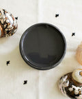 Black Sands Silk All-In-One paint is perfect for painting kitchen cabinets, bathroom cabinets and painting furniture. Open Jar of Black Sand Silk All in one mineral paint staged on a white cloth with black X's. White and gold conch shells on either side of open jar with white and orange seashell next to conch shell.