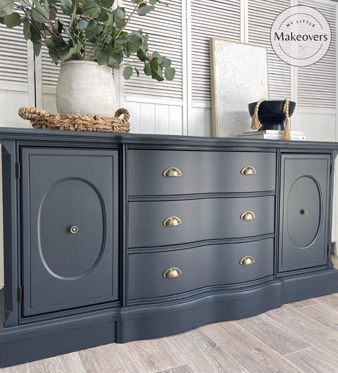 Black Sands Silk All-In-One paint is perfect for painting kitchen cabinets, bathroom cabinets and painting furniture. Dresser with gold hardware painted in Black sand Silk all in one mineral paint. Staged in front of  semi-panel wall, on top of furniture  a white vase and faux leaves on top of woven basket with handles on left side of dresser. Right side has tall black bowl with tan tassels hanging out, behind is a white picture framed.